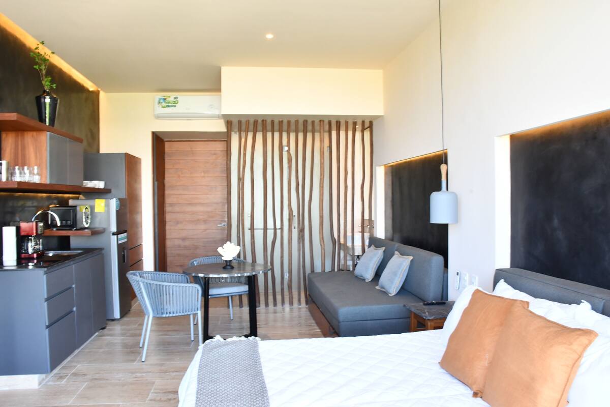 Una habitación de hotel moderna con kitchenette, zona de comedor y sofá cama.