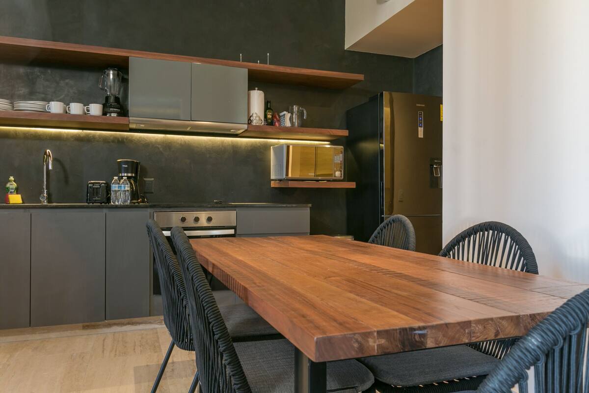 Una cocina moderna con una mesa de comedor de madera, sillas negras y electrodomésticos integrados.