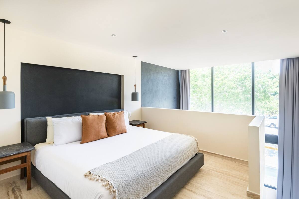 Un dormitorio moderno con una cama grande, una mesita de noche, una lámpara colgante y un ventanal con cortinas.