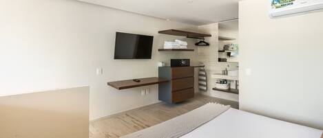 Una habitación de hotel moderna con una cama, un televisor montado en la pared, un aparador de madera y un estante empotrado con toallas.