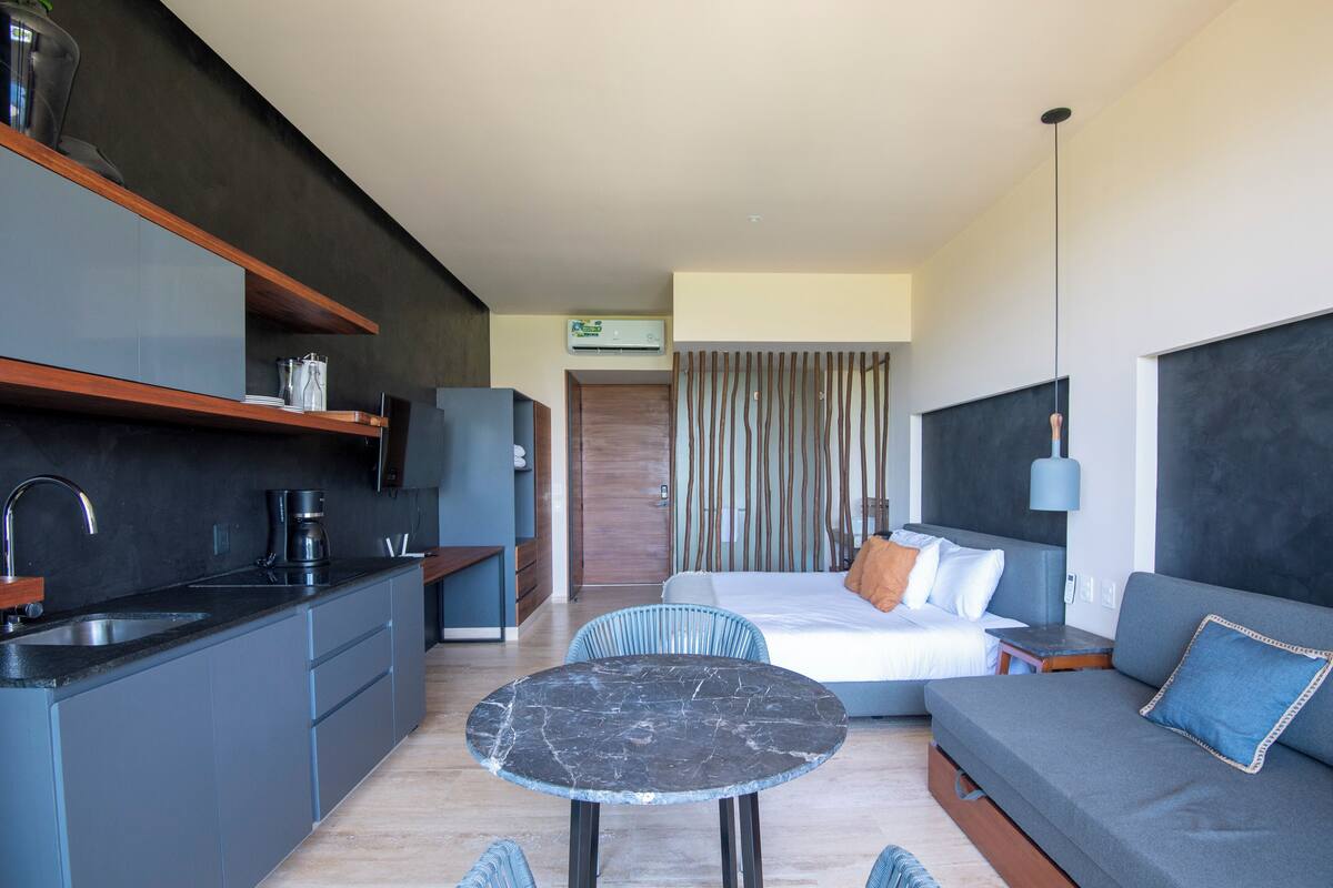 Una habitación de hotel moderna con área de cocina, una mesa de comedor, un sofá y una cama.