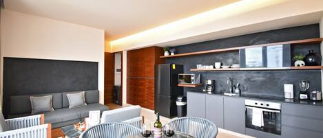 Cocina moderna con armarios grises, un refrigerador negro y un horno empotrado. Cuenta con un comedor con una mesa redonda y sillas, y un sofá gris con cojines.