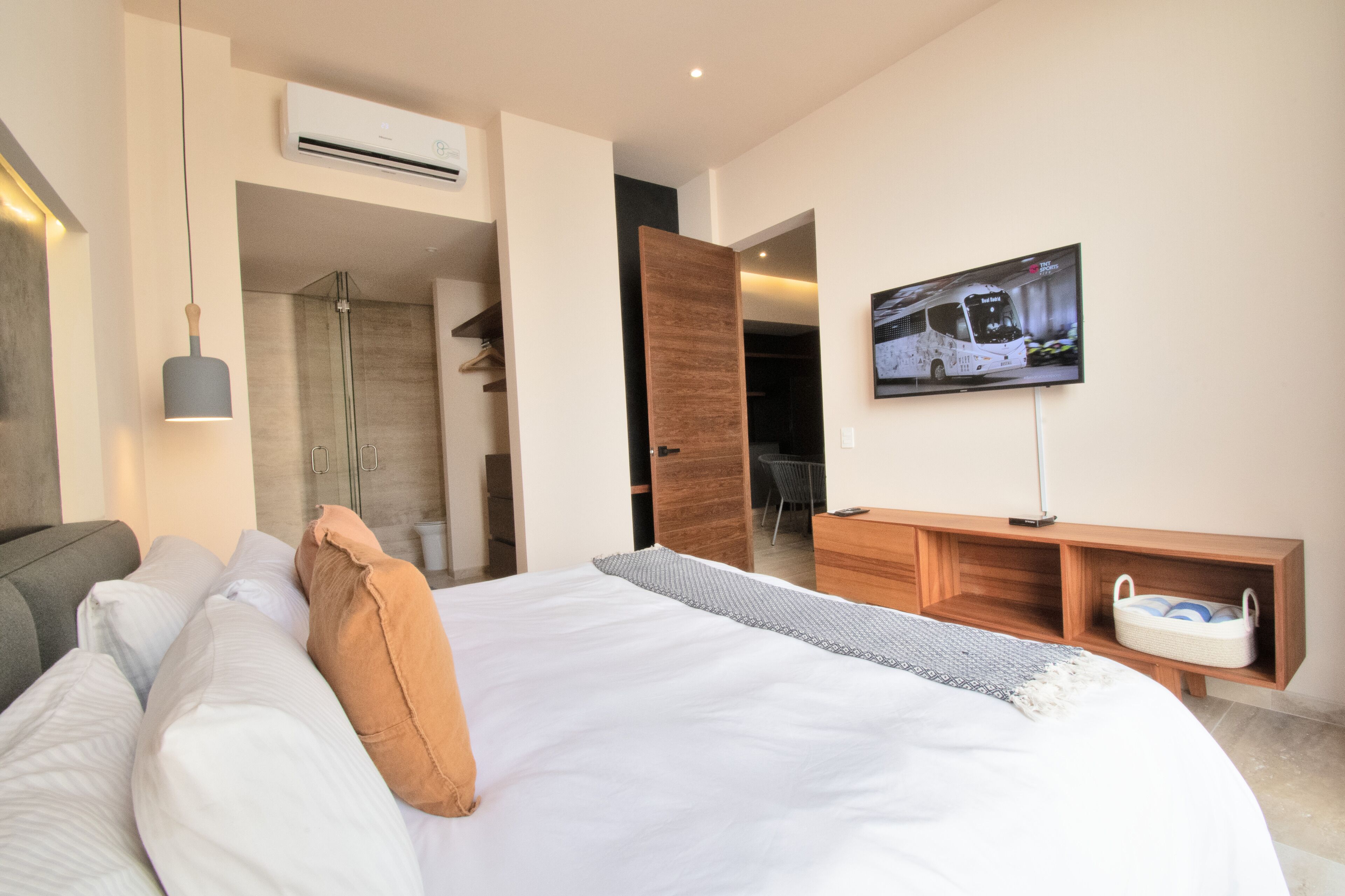 A modern hotel room with a large bed, a TV mounted on the wall, a wooden console table, and a shower area.