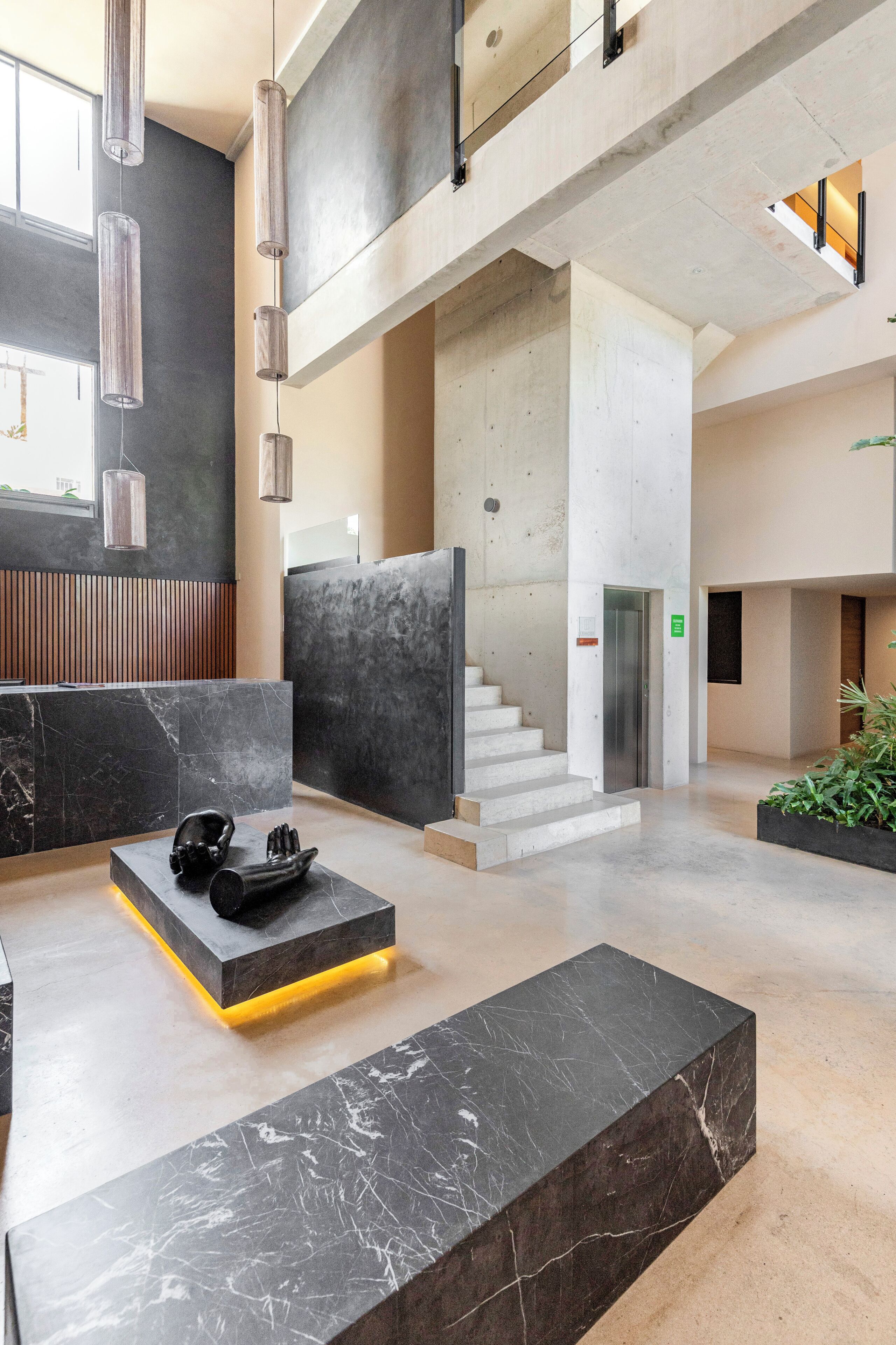 A modern lobby with a marble reception desk, a staircase, and hanging pendant lights.
