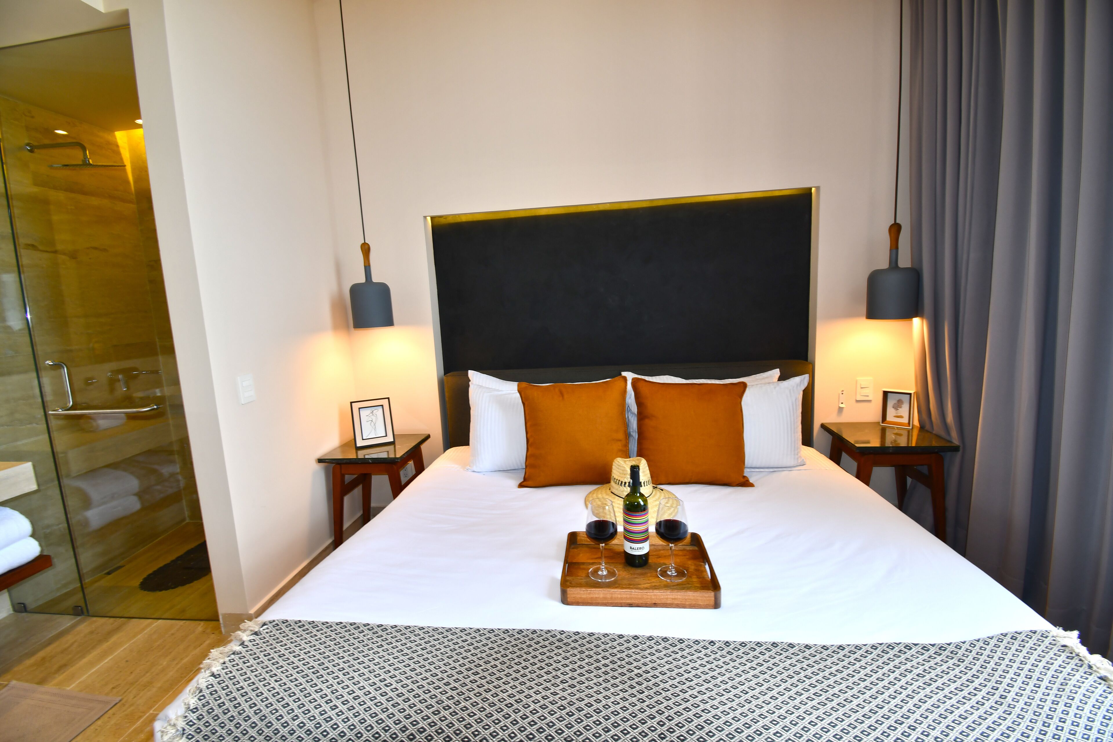 A hotel room with a large bed, two bedside tables, a nightstand, a glass shower enclosure, and a wooden floor.