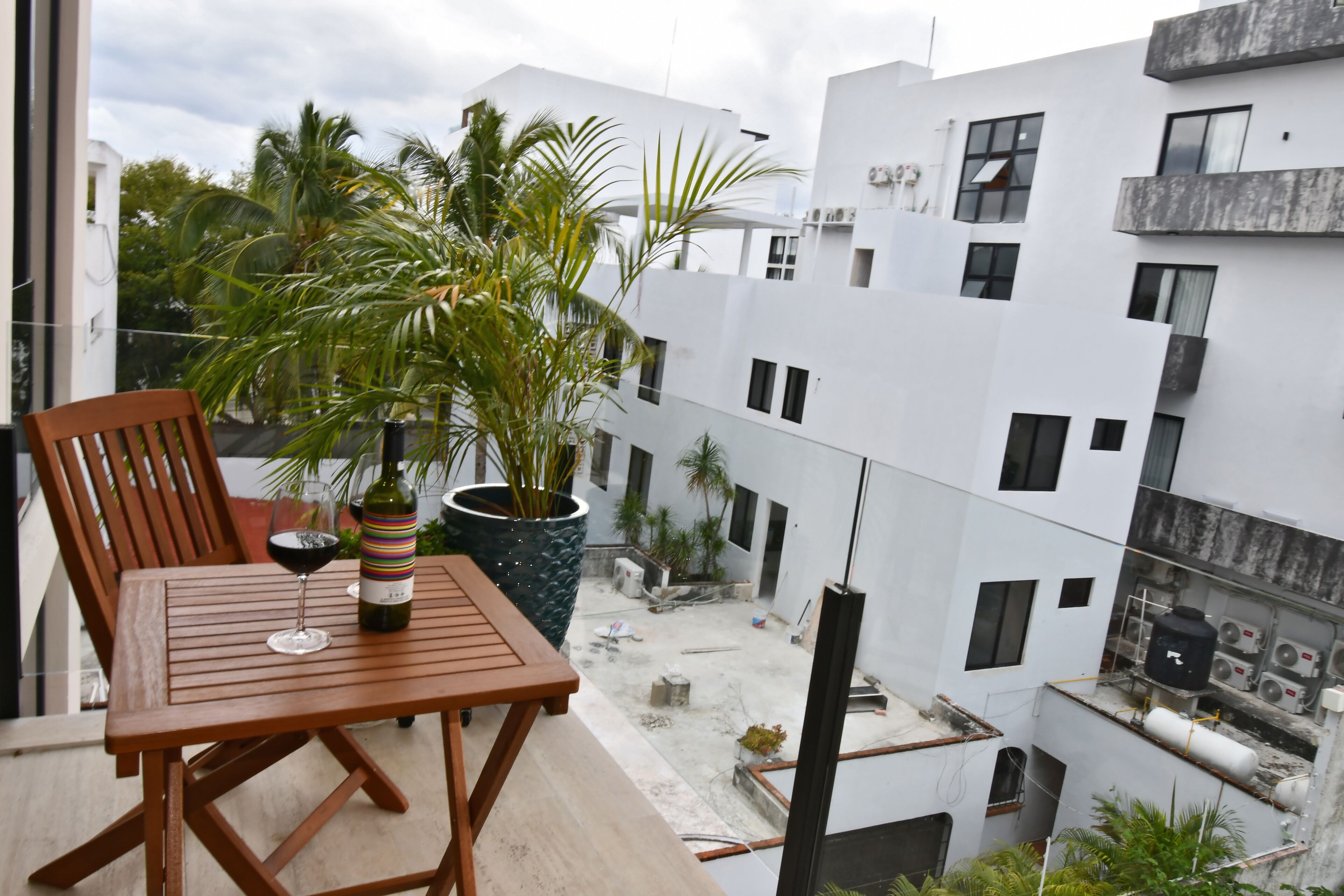 A balcony with a wooden table, a potted plant, and a bottle of wine.