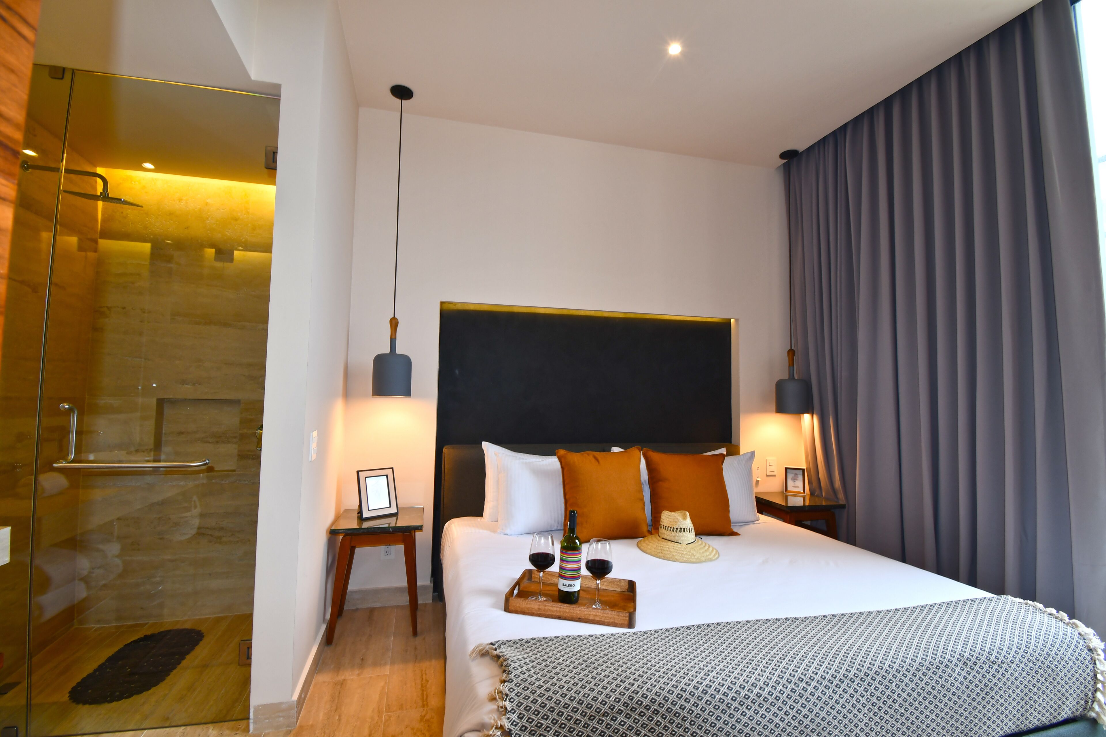 A modern hotel room with a large bed, a bedside table, a nightstand, a headboard, and a shower area.
