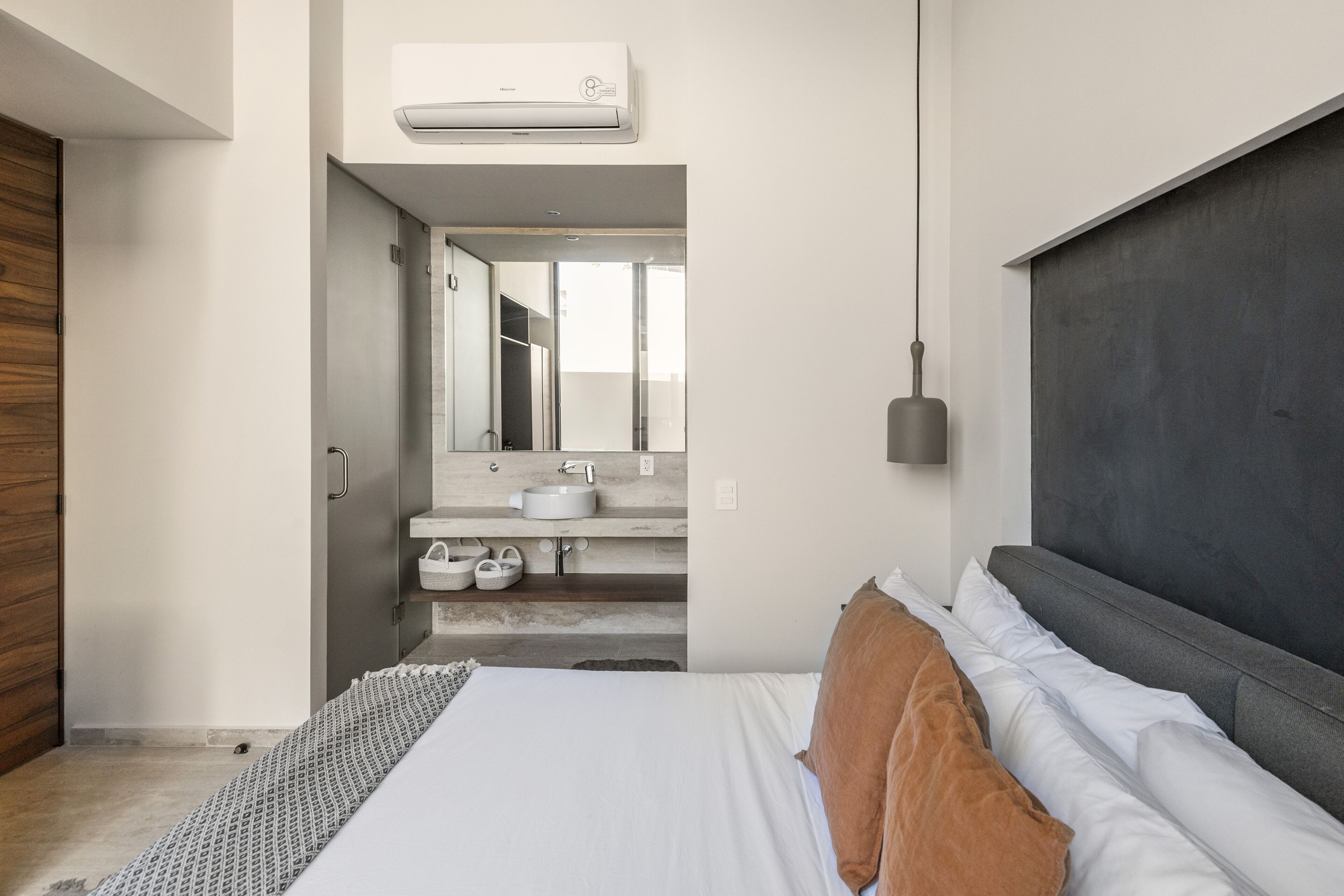 A modern bedroom with a large bed, a dark headboard, a bedside table, and a mirror.
