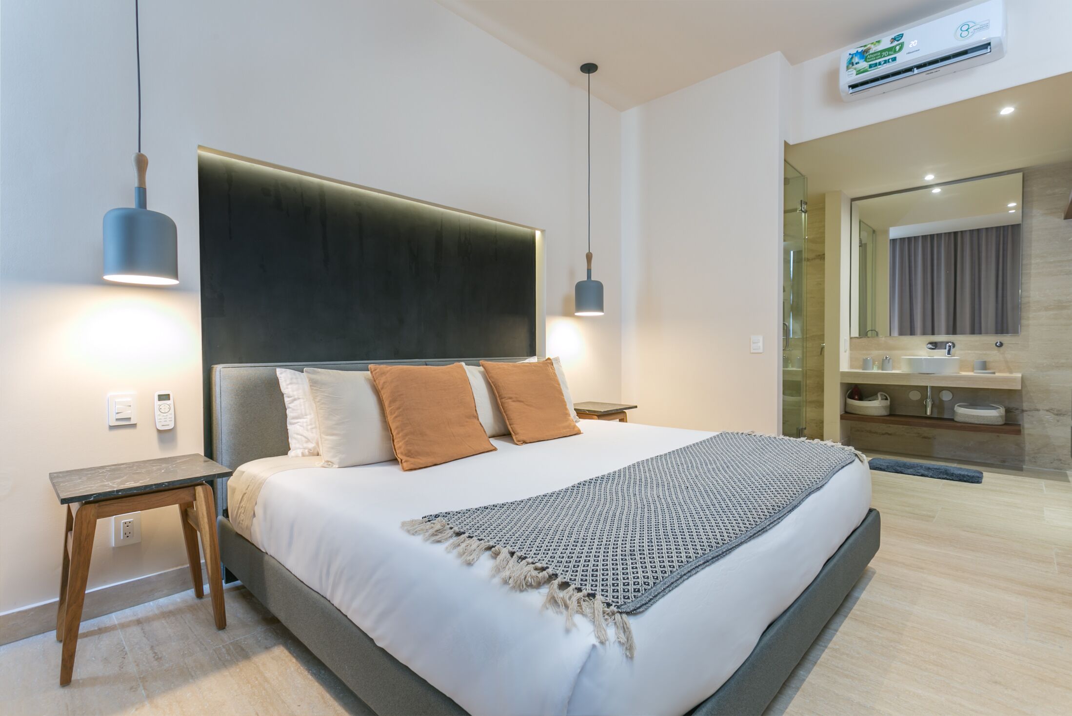 A modern hotel room with a large bed, bedside lamps, a bedside table, and a bathroom visible through an open door.