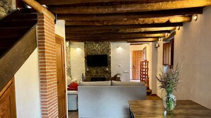 A cozy living room with a stone fireplace, a comfortable sofa, and a dining table. - Rural house, ideal for families in the middle of nature. (Júzcar)