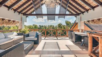 Relax in a serene outdoor space with wicker sofas and chairs, surrounded by lush greenery and a thatched roof.