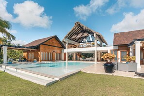 Un resort moderno con piscina, estructuras de madera y un pabellón de techo de paja.