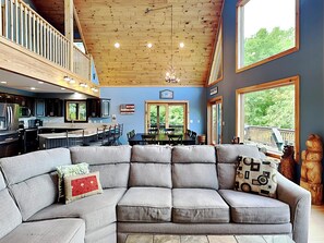 A spacious living area with a gray sectional sofa, a dining table, and a kitchen in the background.