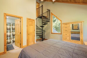 A bedroom with a large bed, a wooden dresser, a mirror, and a spiral staircase.