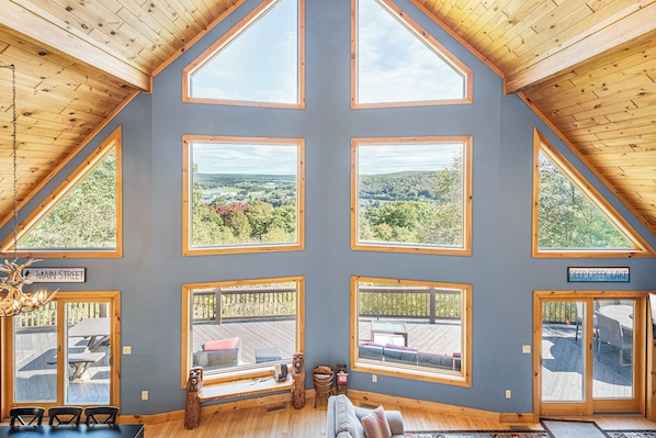 A spacious room with large windows offering views of a forested area and a lake.