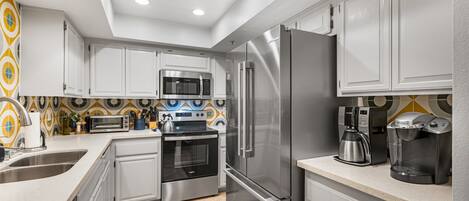A modern kitchen with stainless steel appliances, white cabinets, and a patterned backsplash.