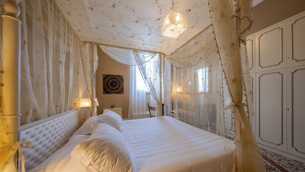 Cama bem arrumada com lençóis brancos, cabeceira com design acolchoado e cortinas translúcidas estampadas com flores.