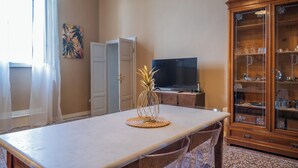 Uma sala de estar com uma mesa de jantar, uma televisão, um armário e um quadro na parede.