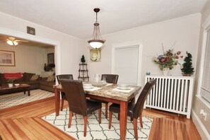 Uma sala de jantar com uma mesa posta para quatro pessoas, rodeada por cadeiras, um candelabro e um ornamento na parede.