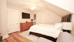 Quarto com cama, penteadeira, ventoinha no teto e televisão na parede.