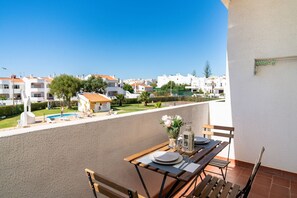 A balcony with a wooden table set for dining, overlooking a residential area with white buildings and a swimming pool. - Silchoro - Charming, renovated studio with pool and AC (Albufeira)