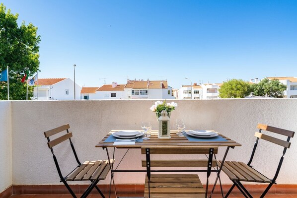 A wooden table set for two with chairs, a vase with flowers, and a lantern on a balcony overlooking a residential area. - Silchoro - Charming, renovated studio with pool and AC (Albufeira)