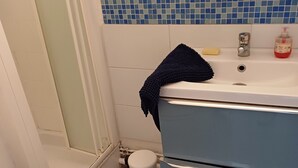 Ein Badezimmer mit blauer Fliesenwand, einem weißen Waschbecken mit blauem Handtuch, einer weißen Toilette und einem blauen Mülleimer.