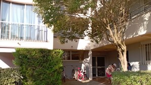 Ein Wohngebäude mit überdachter Eingangspforte, ein Fahrrad ist vor der Fassade abgestellt, und ein Baum befindet sich im Vordergrund.