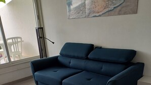 Ein Zimmer mit einem dunkelblauen Sofa, einem kleinen weißen Beistelltisch und einem Fenster mit Blick auf den Strand.