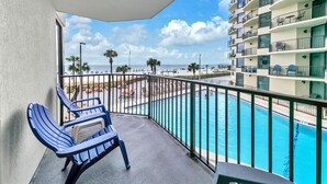 Ein Balkon mit Blick auf einen Pool, Liegestühle und ein Hochhaus im Hintergrund.