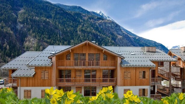 A wooden chalet with multiple balconies and a mountain backdrop.