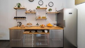 A modern kitchen with stainless steel appliances, wooden countertops, and multiple wall-mounted clocks. - dpaso hostel (Chantada)