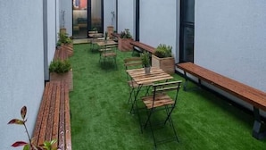 A modern building with a narrow courtyard featuring a green lawn, wooden benches, and potted plants. - dpaso hostel (Chantada)