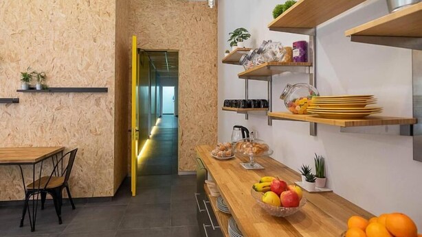 A modern kitchen with wooden cabinetry, a built-in oven, and a long countertop with fruit bowls and kitchen utensils. - dpaso hostel (Chantada)