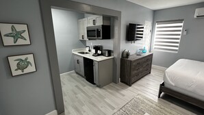 Ein kleines Schlafzimmer mit einem Bett, einer Kommode und einer Küchenzeile, inklusive Mikrowelle und Kaffeemaschine.