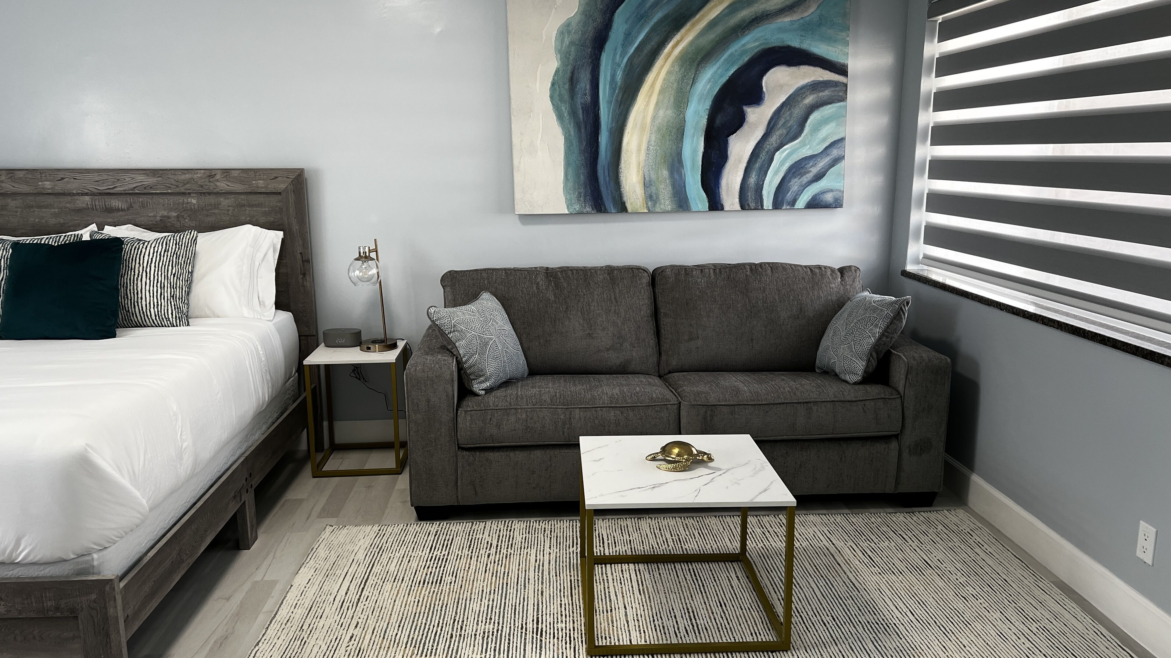 Ein modernes Schlafzimmer mit einem Bett, einem grauen Sofa, einem kleinen Tisch und einem Wandbild.
