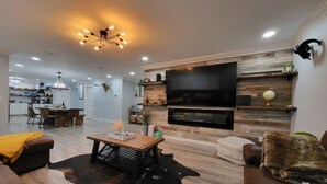 A modern living room with a large flat-screen TV, wooden flooring, a cowhide rug, and a dining area in the background. - The Farmstead- Pool, Hot Tub, Firepit and Farm Fresh Eggs/Animals in Walla Walla (Walla Walla)