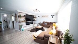 A modern living room with a large flat-screen TV, a brown sectional sofa, and a fireplace. - The Farmstead- Pool, Hot Tub, Firepit and Farm Fresh Eggs/Animals in Walla Walla (Walla Walla)