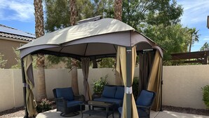 Un patio couvert avec deux chaises bleues rembourrées et une table, situé à côté d’une piscine.