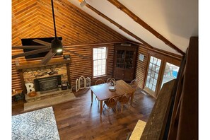 Cozy cabin interior with a central fireplace, dining table, and high ceiling with exposed beams.