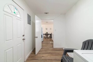 Un couloir étroit avec des portes blanches, un coin repas avec une table et des chaises, et une chaise noire au premier plan.