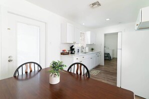 Une cuisine moderne avec des meubles blancs, une table à manger avec des chaises et une plante en pot posée sur la table.