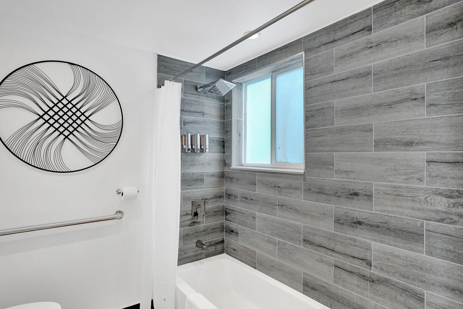 A modern bathroom with a bathtub, a shower, and a window providing natural light.