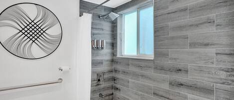 A modern bathroom with a bathtub, a shower, and a window providing natural light.