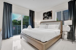 Une chambre moderne avec un grand lit, une table de chevet, une commode et une vue sur la verdure.