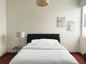 A hotel room with a bed, a bedside table with a lamp, and two wall-mounted artworks.
