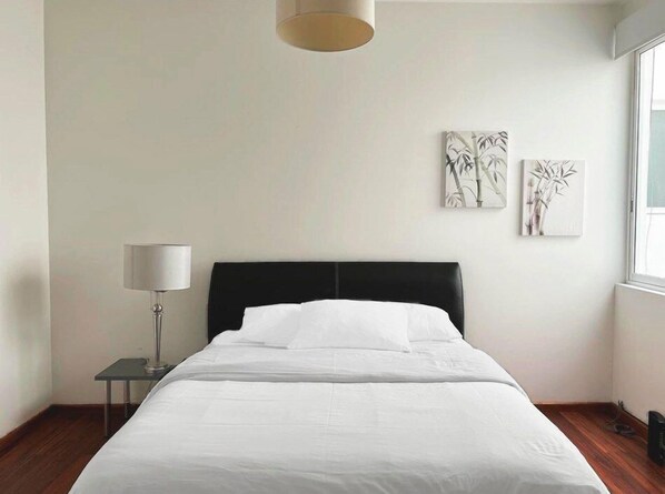 A hotel room with a bed, a bedside table with a lamp, and two wall-mounted artworks.