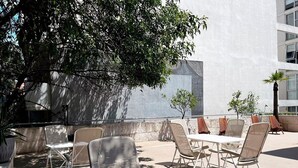 An outdoor seating area with tables and chairs, surrounded by a low stone wall and trees. - Condesa Residence Amsterdam F (Ciudad de México)