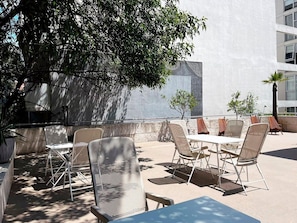 Un espace extérieur aménagé avec des tables et des chaises, entouré d’un petit muret en pierre et d’arbres.