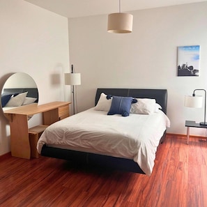 Une chambre à coucher avec un lit, une table de chevet, une lampe et un miroir.